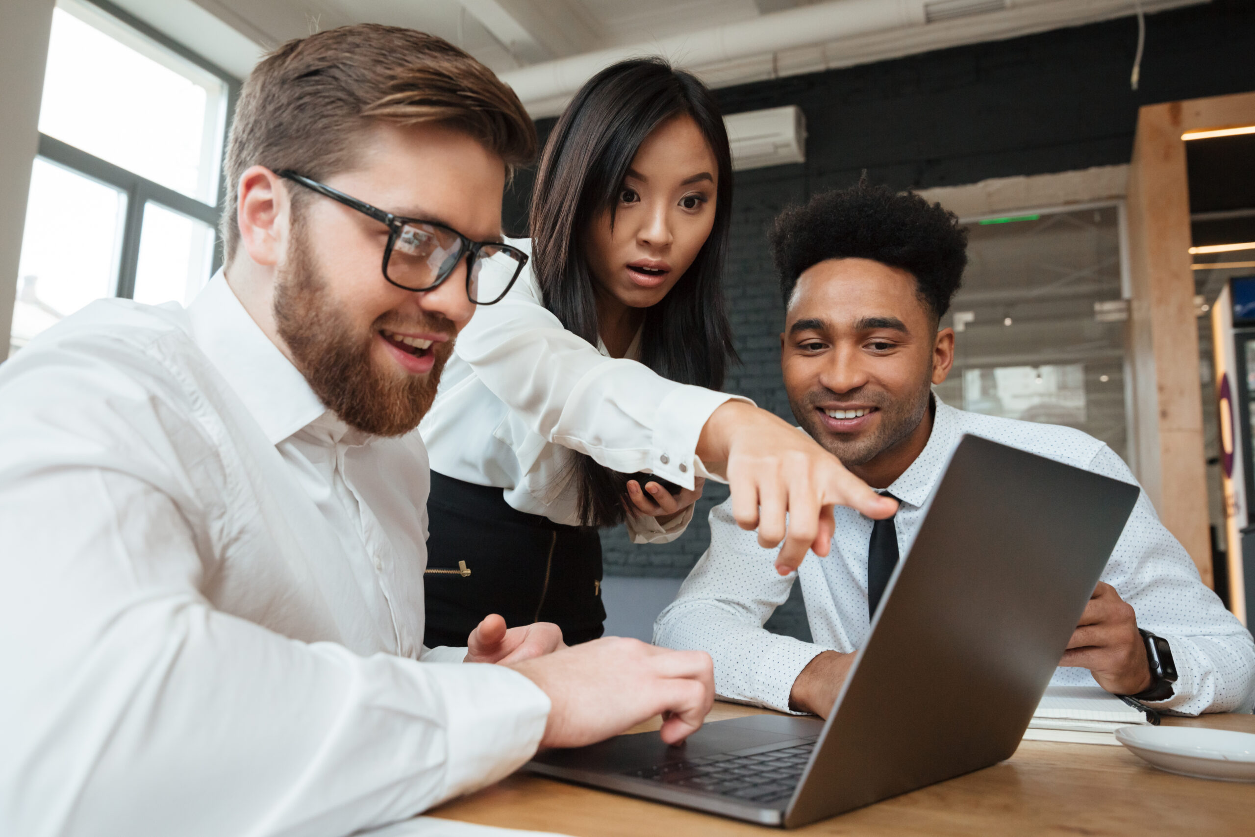 Photo Of Shocked Asian Woman Showing Display Of Laptop Computer To Her Colleagues Indoors Coworking. Looking Aside.